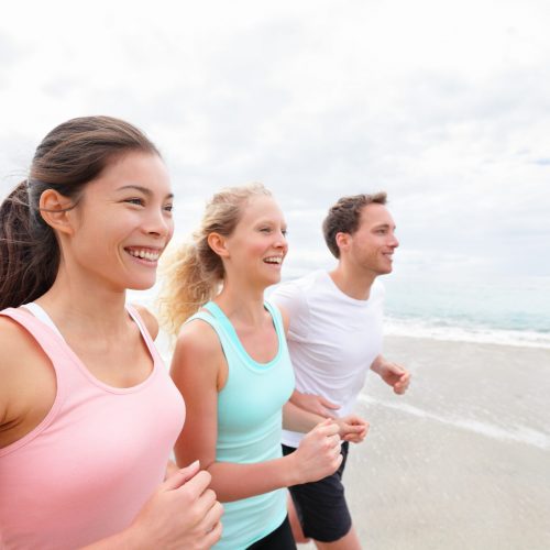 Group running on beach jogging. Exercising runners and friends training outdoors living healthy active lifestyle. Multiracial fitness runner people working out together outside smiling happy.